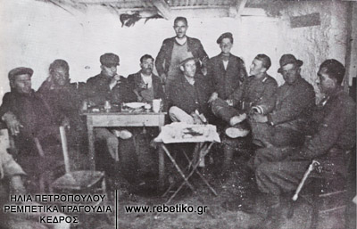 Μία παρέα στην ταβέρνα των αδερφών Αποστόλη και Γιάννη Κυριάκογλου, στην λεωφόρο Ποσειδώνος. Στην μέση ο καπετάν Αντρέας Ζέπος (με καβουράκι) και δίπλα του ο ιταλός γρεναδιέρος Angelo Marzari (1941 ή 1942)